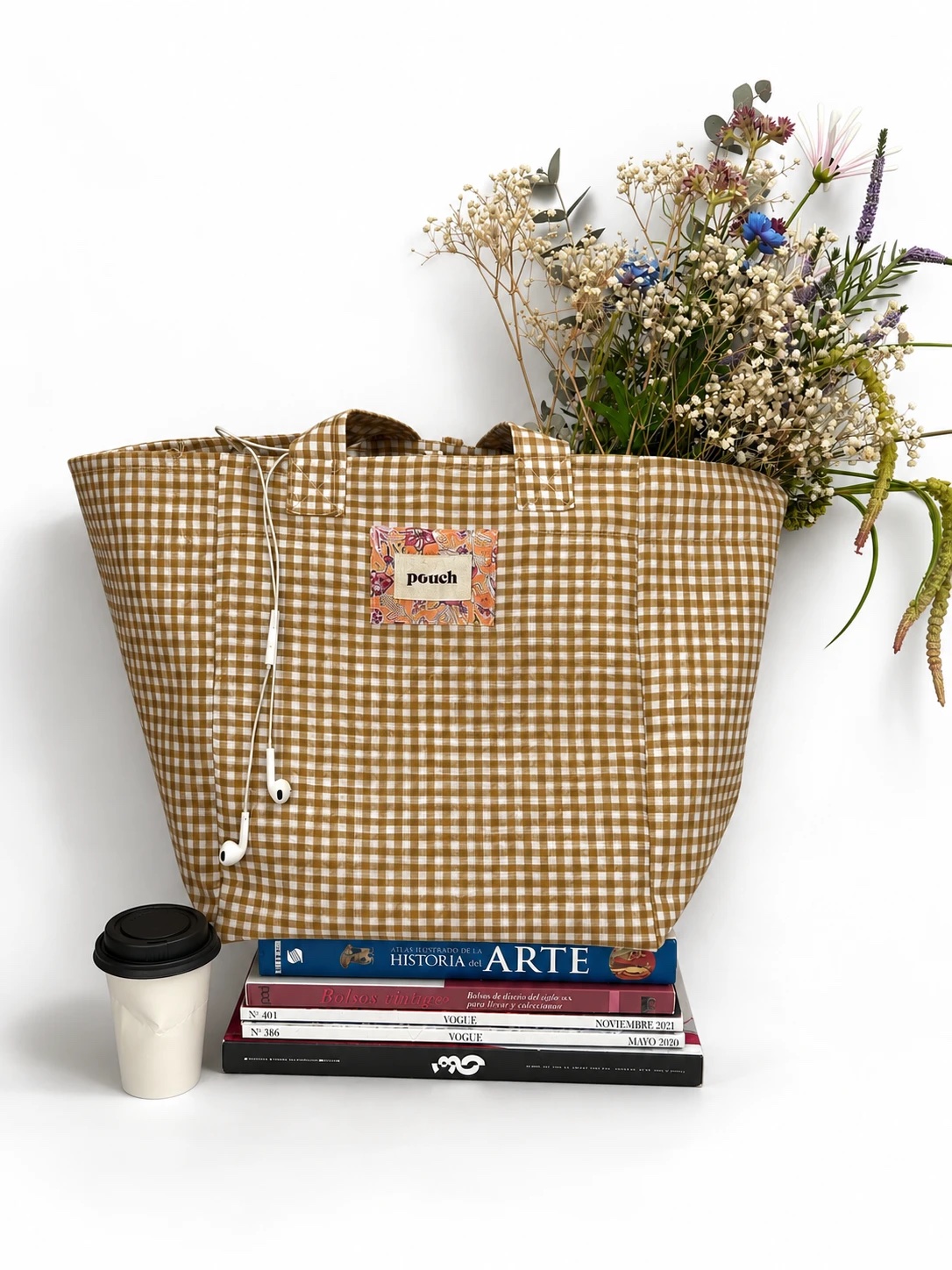 Bolso Lirio cuadros con flores, apoyado sobre libros y revistas junto a un café