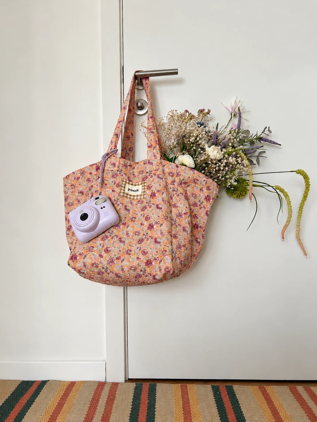 Bolso Lirio floral colgado de una puerta, con flores y una cámara instantánea