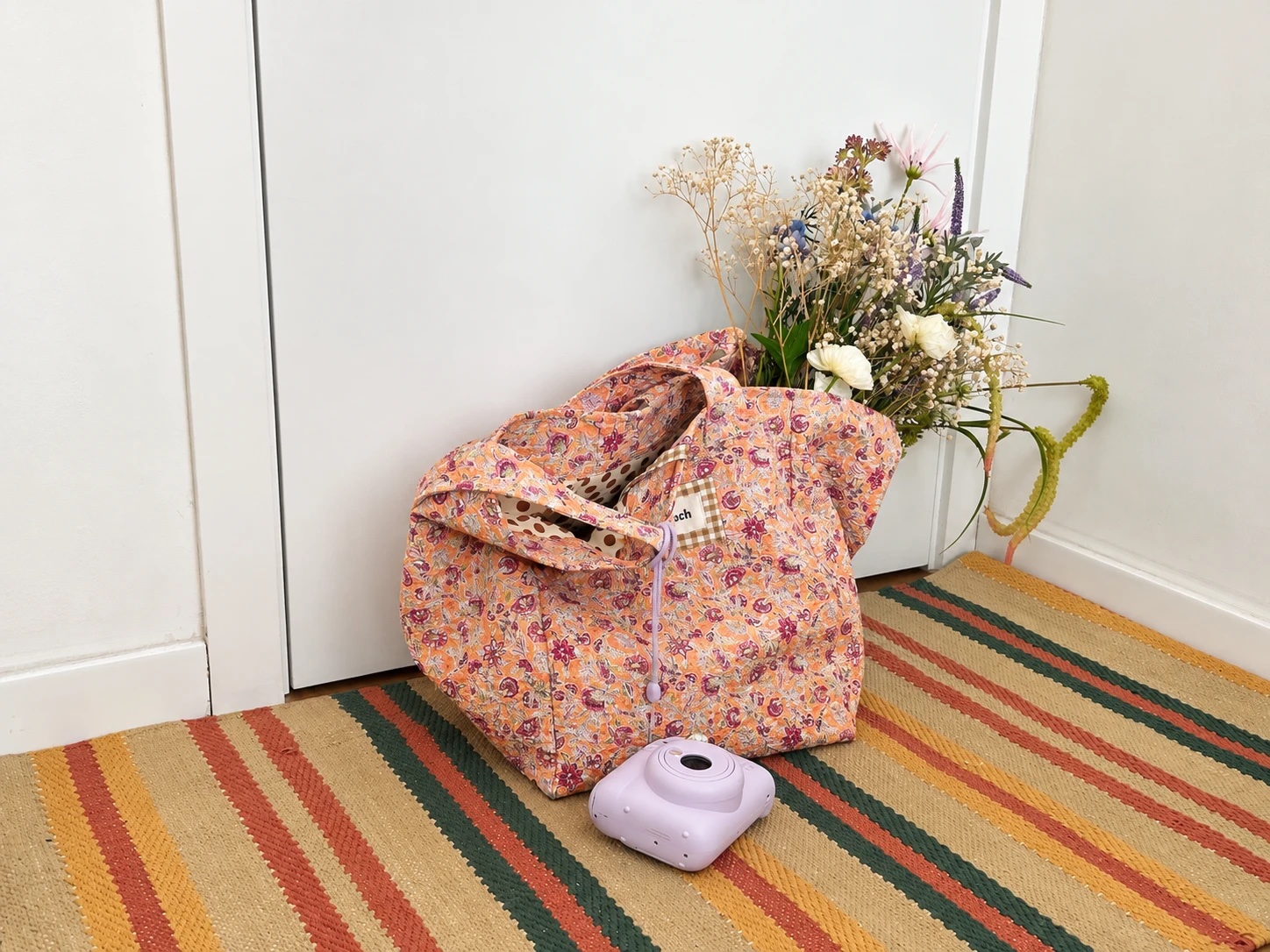 Bolso Lirio floral con flores secas y una cámara instantánea sobre una alfombra a rayas